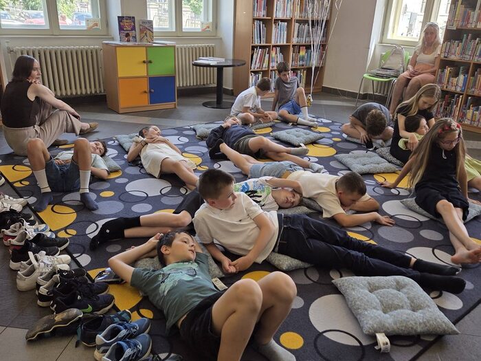 Deti ležia na koberci a počúvajú čítanie z knihy